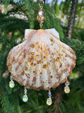 Decorative shell with gold glitter and crystal beads hanging against a green leafy background