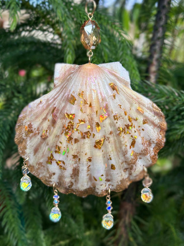 Decorative shell with gold glitter and crystal beads hanging against a green leafy background